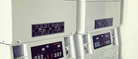 A stack of white washing machines with control panels and a notice label.