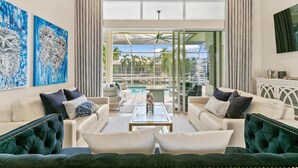 A spacious living room with a view of a pool and palm trees. There are two sofas and a coffee table in the center. - Marco Island Waterfront Single-Story Home w/ Direct Gulf Access (Marco Island)