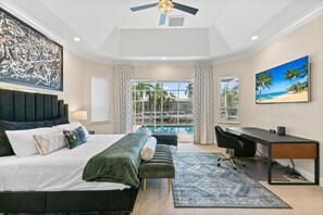 Quarto de hotel moderno com uma cama grande, uma mesa de trabalho e vista para uma piscina e palmeiras.