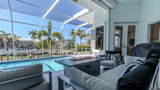 A poolside area with a fire pit, outdoor seating, and a view of the pool and palm trees. - Marco Island Waterfront Single-Story Home w/ Direct Gulf Access (Marco Island)