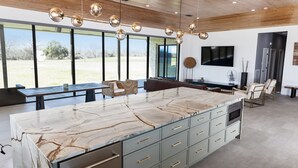 A spacious kitchen with a large marble island, modern pendant lighting, and a view of the outdoors. - Breathtaking modern 100 acre ranch on the Colorado River. Weddings available (Smithville)