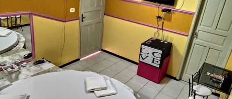 Habitación de hotel con una mesa redonda, una pequeña zona de bar, un televisor montado en la pared y una puerta con una franja rosa.
