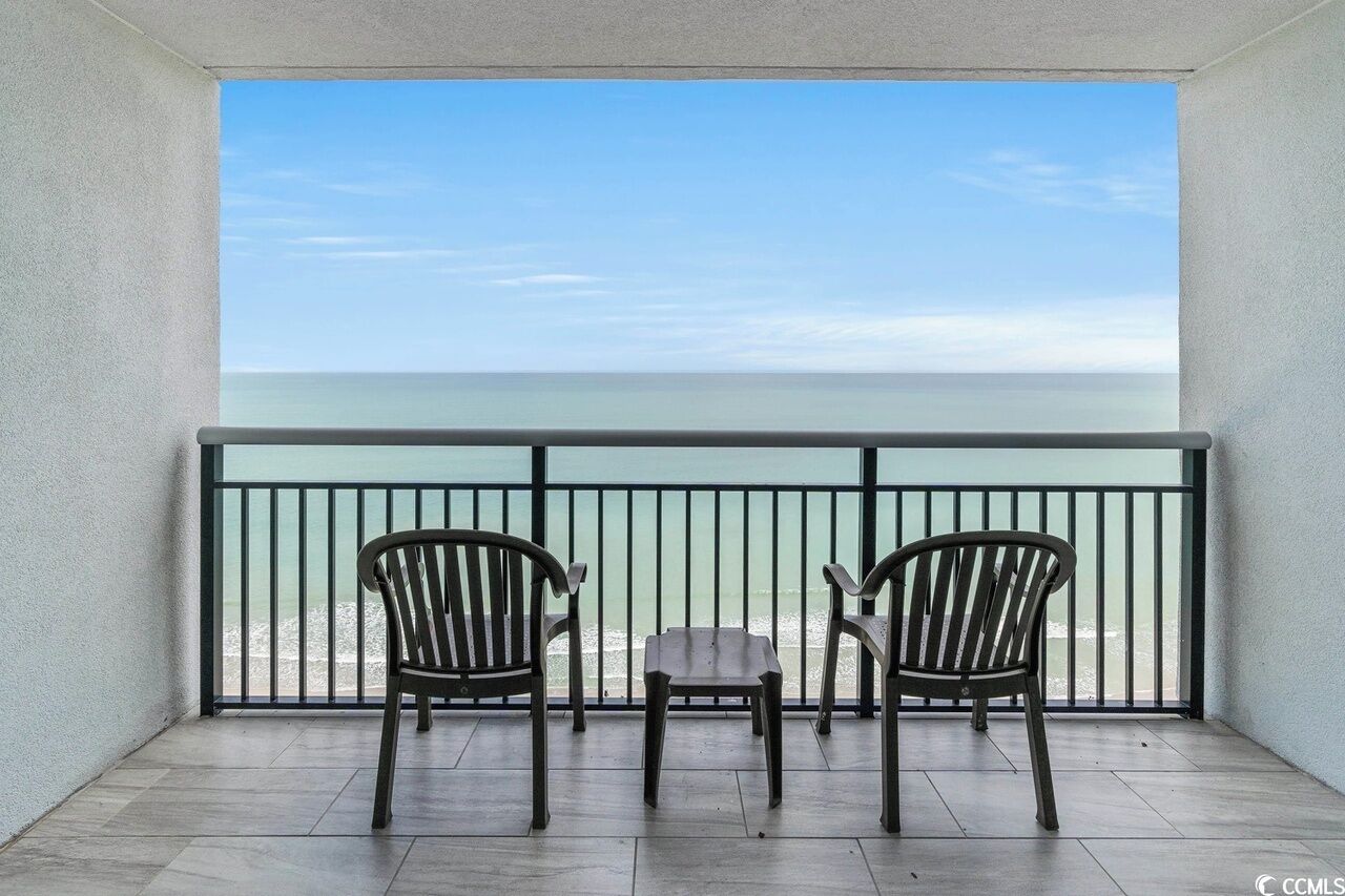 A balcony with two wooden chairs and a small table, overlooking a calm sea.