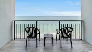 A balcony with two wooden chairs and a small table, overlooking a calm sea.