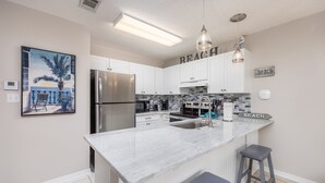 A kitchen with white cabinets, a marble countertop, a stainless steel refrigerator, a sink, and two bar stools. - Private Beach Access! Complementary Beach Service! (Miramar Beach)