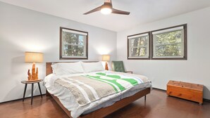 A bedroom with a wooden bed, two bedside lamps, a ceiling fan, and two windows with blinds.