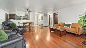 A spacious living room with a leather sofa, a wooden coffee table, and a tan couch. There is a dining area with a table and chairs in the background.