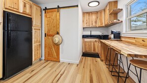A kitchen with wooden cabinets, a black refrigerator, a sliding door, and a window with a view.
