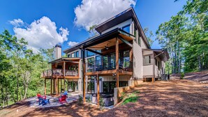 A modern two-story house with a deck, outdoor seating, and a hot tub.
