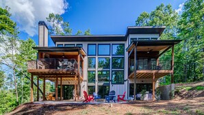 A modern two-story house with large windows, a covered patio, and outdoor seating.