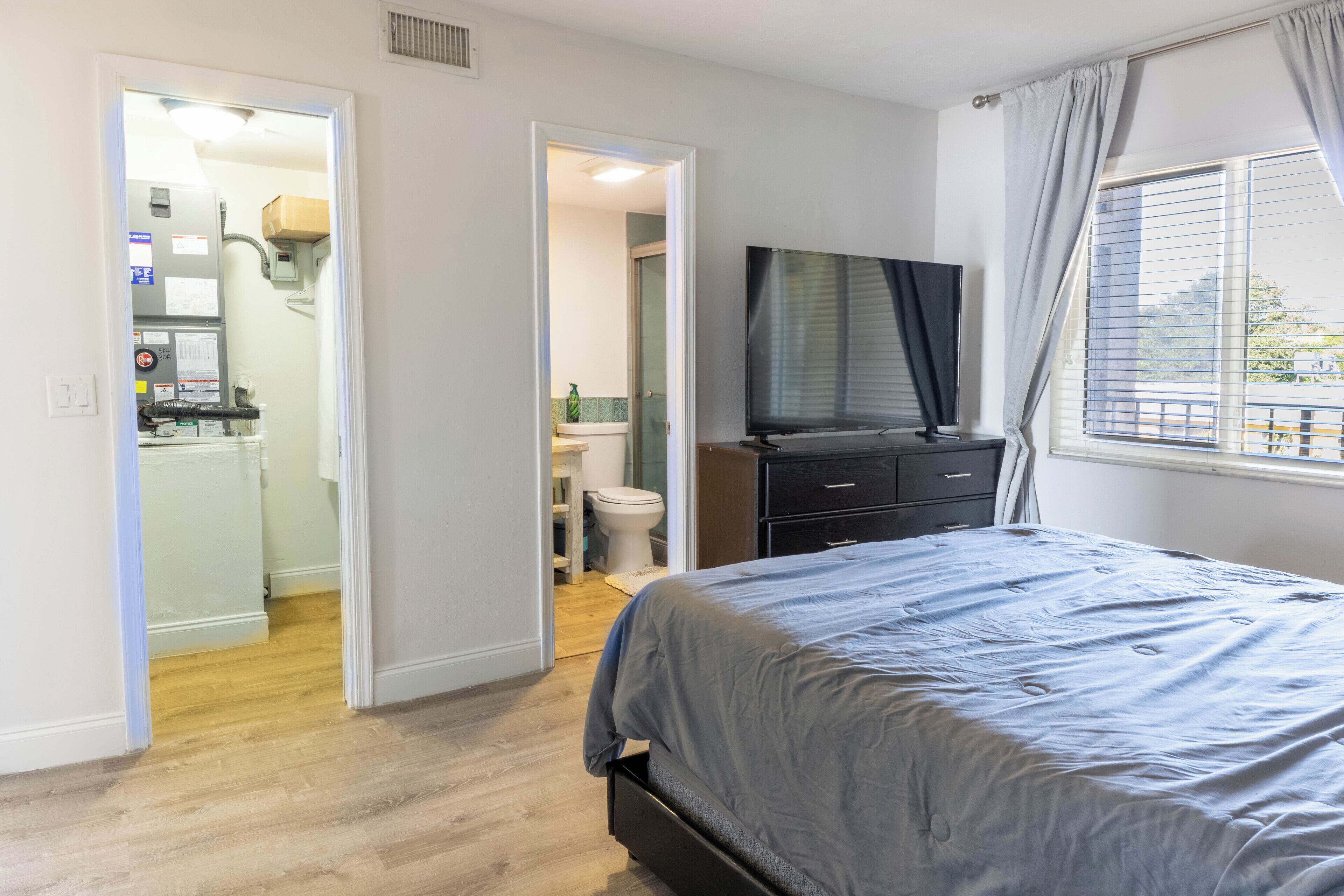 A bedroom with a bed, a TV, and a window with curtains.