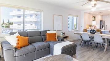 A modern living room with a grey sectional sofa, a dining table with chairs, and a ceiling fan.