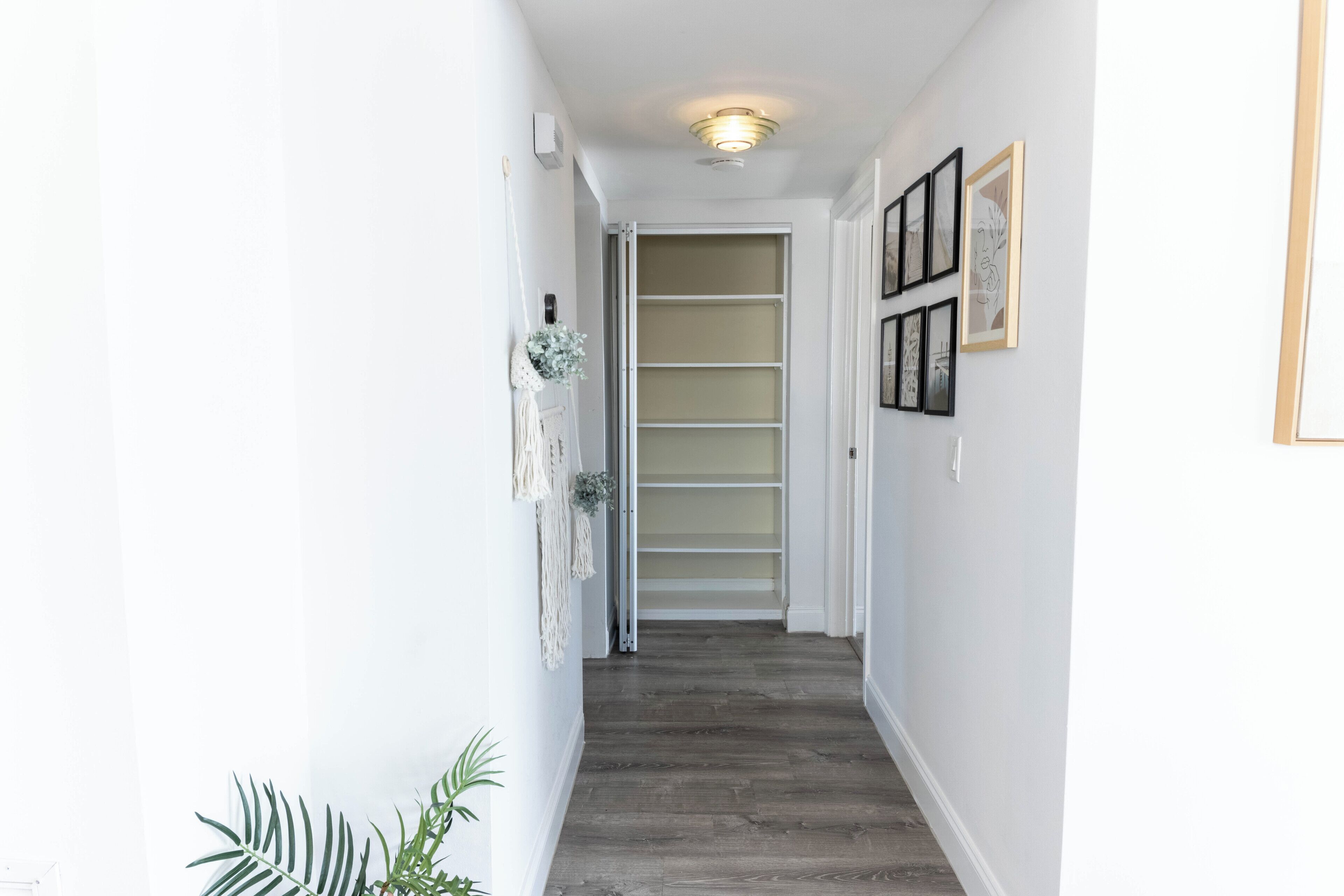 A narrow hallway with a wooden floor, white walls, and a door leading to a room with a sliding door.