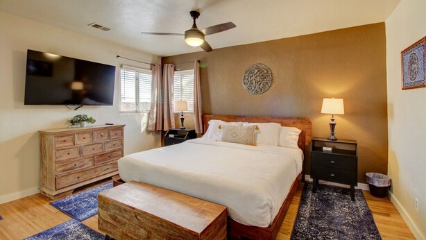 Een slaapkamer met een groot bed, een houten dressoir, een nachtkastje, een plafondventilator en een aan de muur bevestigde televisie.