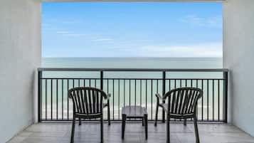 A balcony with two wooden chairs and a small table, overlooking a calm sea.
