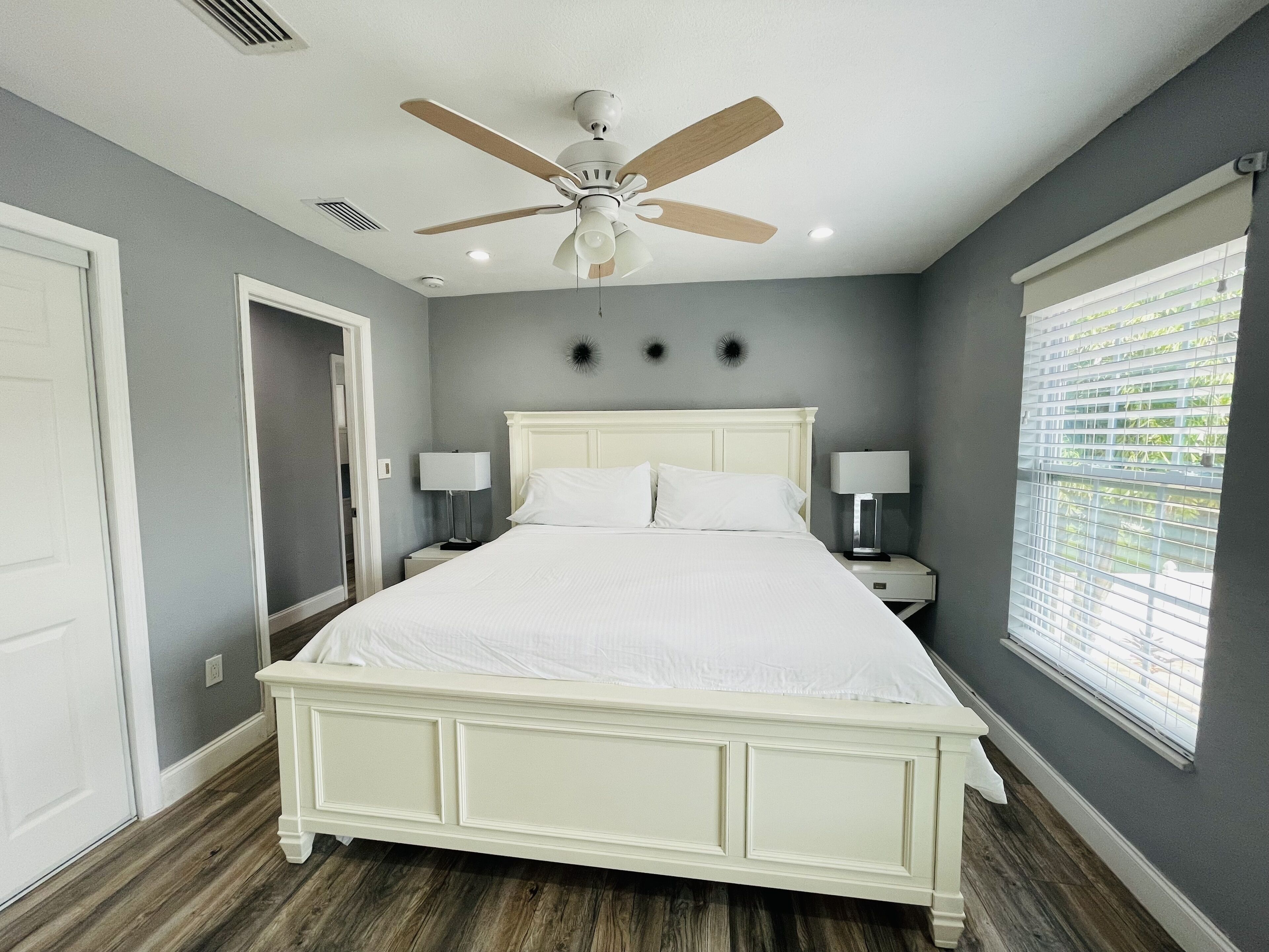 A bedroom with a bed, two bedside tables, a ceiling fan, and a window with blinds.