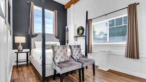 A bedroom with a four-poster bed, a bedside table with a lamp, and a window with curtains. - Shamrock by the Sea Hot Tub Arcade Basketball Court & Beach Fun (Wells)