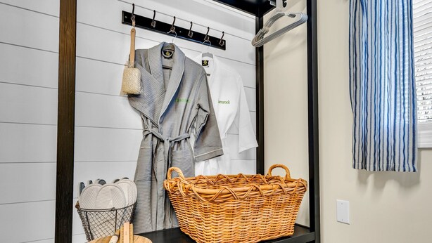 A bathroom with a black countertop, a wicker basket, a wooden bowl, and a rack with towels and a robe. - Shamrock by the Sea Hot Tub Arcade Basketball Court & Beach Fun (Wells)