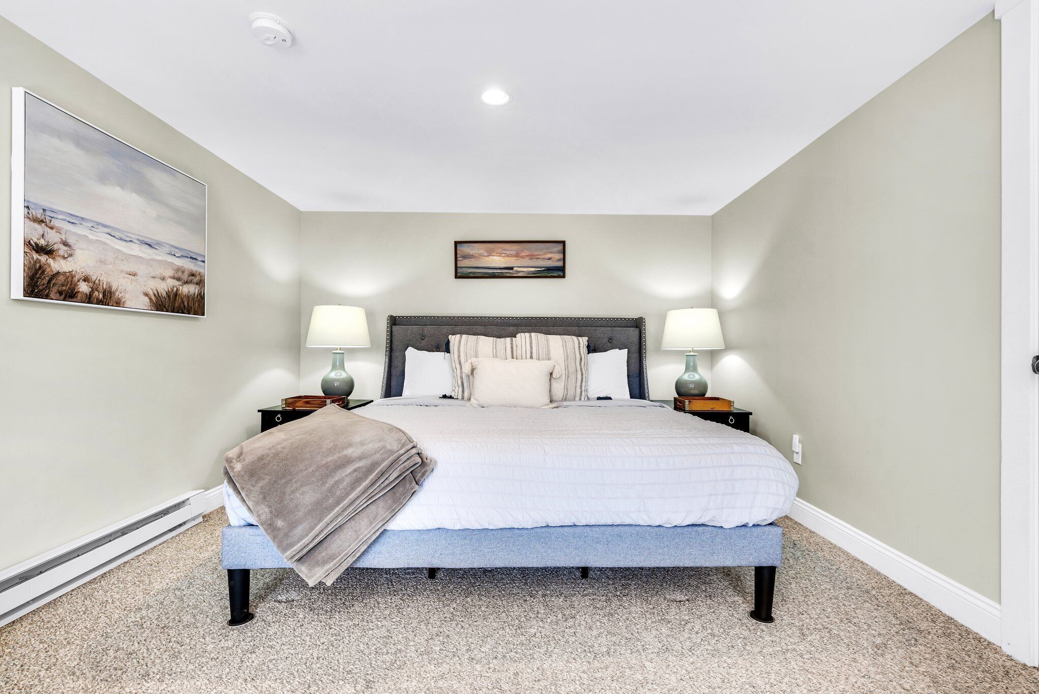 A bedroom with a bed, two bedside tables, two lamps, a headboard, and two wall-mounted pictures.
