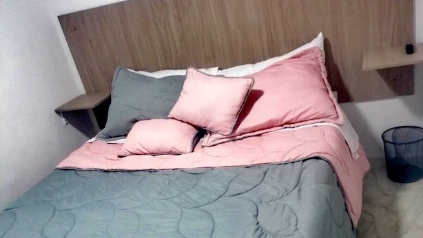 A bed with a grey quilt and pink pillows, a wooden headboard, and a small bedside table with a lamp. - hotel 51b (Bogotá)