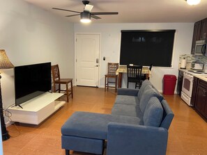 Un salon équipé d’un téléviseur à écran plat, d’un ventilateur de plafond, d’un canapé et d’un coin repas avec des chaises et une table.