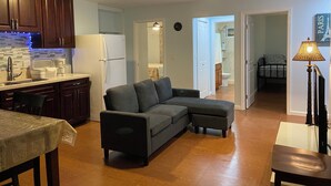 A modern living room with a sectional sofa, a dining table, and a kitchen area with wooden cabinets and a refrigerator. - 2bedrm/1bathrm, near shopping center and freeway  (Honolulu)
