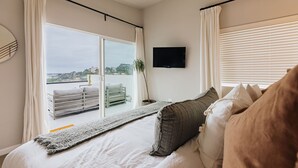 A bedroom with a bed, a TV, and a view of the city through large windows. - Brand NEW4BR, Views, Family Friendly (San Diego)