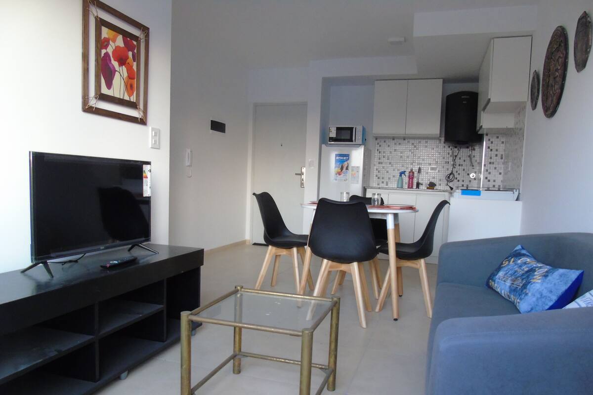 Un salon moderne avec un téléviseur à écran plat, une table basse et un canapé agrémenté d’un coussin décoratif.