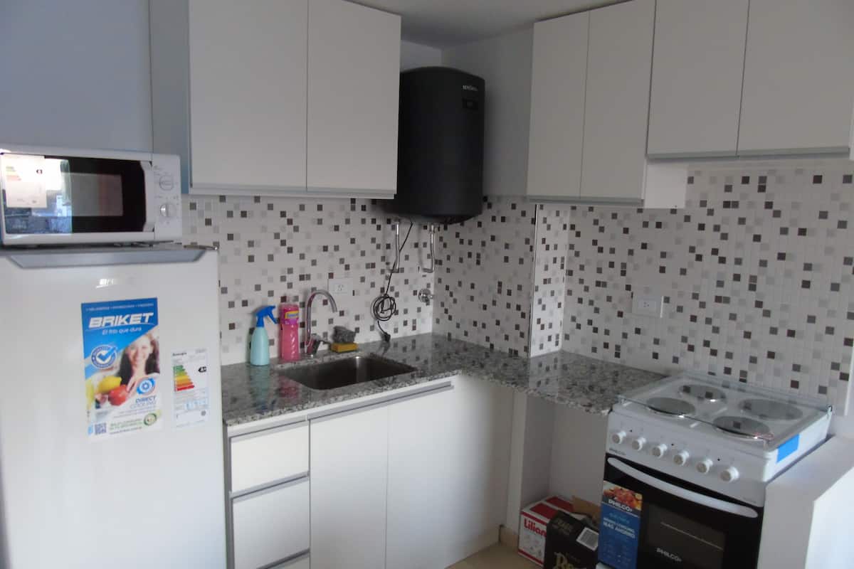 Une cuisine avec des meubles blancs, un four à micro-ondes, un évier, une cuisinière à gaz et un dosseret carrelé.