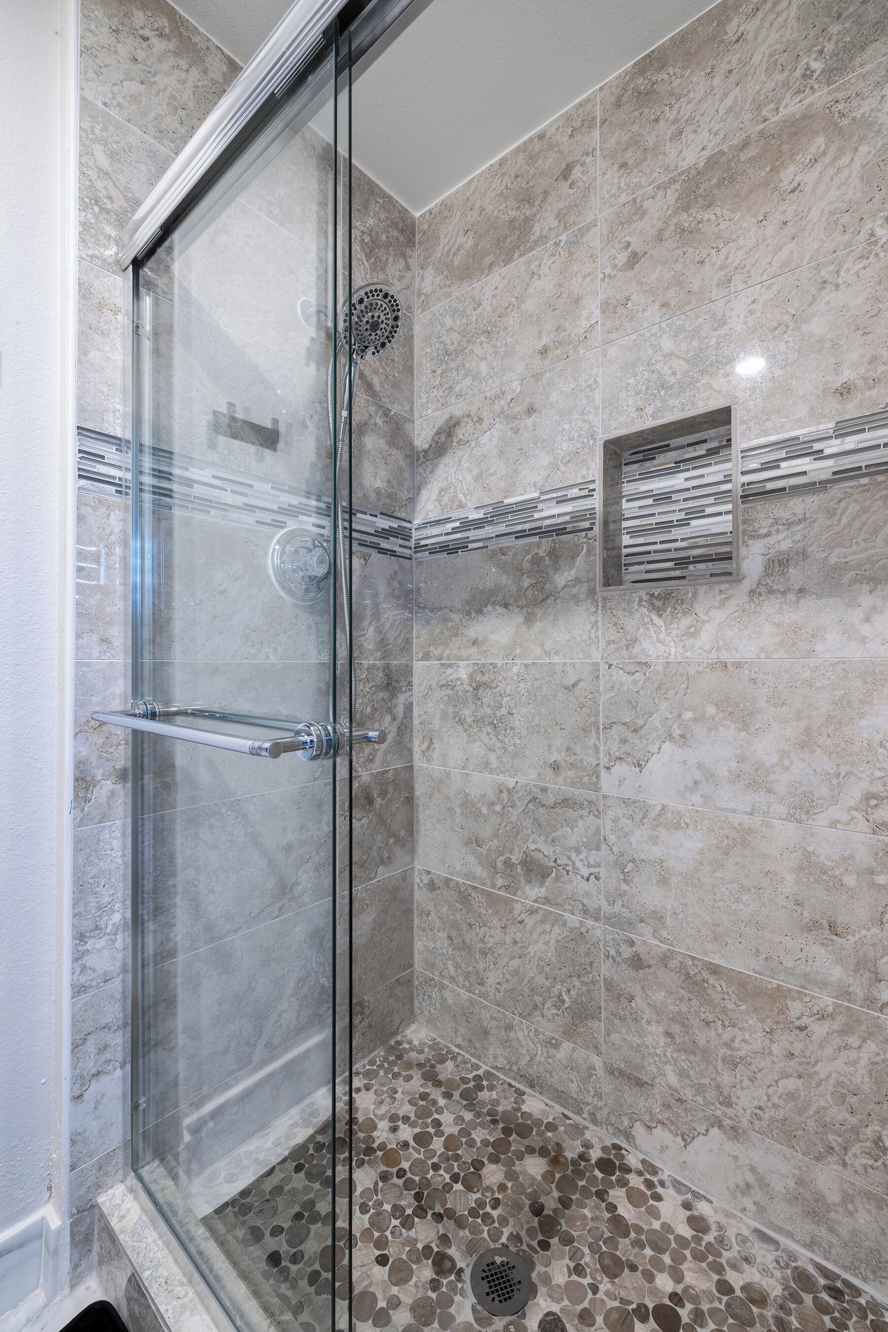 Une douche fermée par des parois de verre, dotée d’un sol en marbre et d’une étagère intégrée.