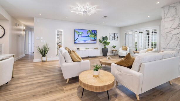 Een moderne woonkamer met witte banken, een ronde houten salontafel en een televisie waarop een strandscène te zien is.
