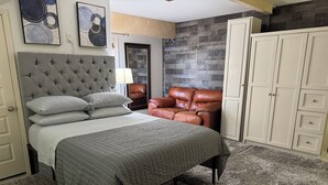 Un dormitorio con cama de cabecera capitonada, un sillón de cuero y un armario.