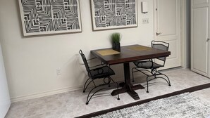 Un área de comedor con una mesa de madera oscura, dos sillas, una planta en maceta y dos obras de arte abstracto en la pared.