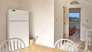 Ein Zimmer mit einem weißen Kühlschrank, einem Esstisch mit Stühlen und Blick auf einen Balkon mit einem Bett.