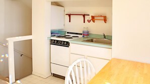 A compact kitchen with a stove, sink, and wooden table. - Sea Forever Condo at Maris Stella (Ocean Shores)