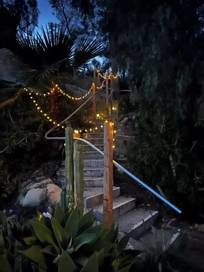 Eine Treppe mit Lichterketten, umgeben von Grünpflanzen und einer Steinmauer.