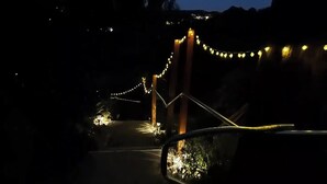 Vista nocturna de una carretera con luces de adorno y un retrovisor de coche reflejando las luces.