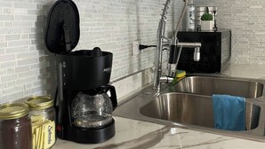A kitchen with a white brick backsplash, a stainless steel sink, a coffee maker, and a bottle of hand soap.