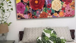 A bedroom with a bed, pillows, a nightstand, and a wall-mounted painting of flowers.