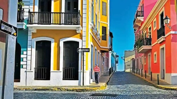A cobblestone street lined with colorful buildings, a pedestrian, and a sign indicating a transit stop.