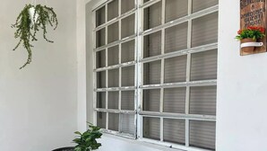 A small patio area with a round table and two wicker chairs, a hanging plant, and a window with blinds.