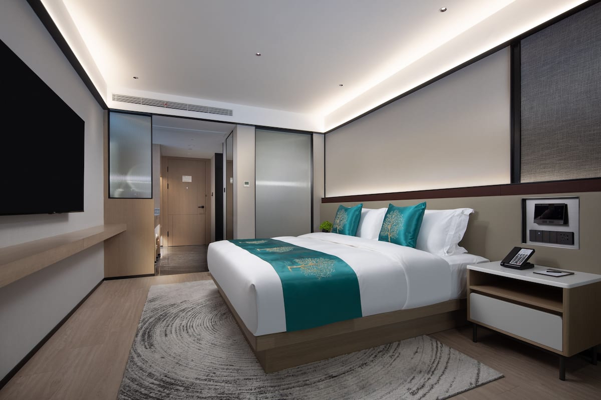 Quarto de hotel moderno com cama grande, mesas de cabeceira, televisão e closet espaçoso.