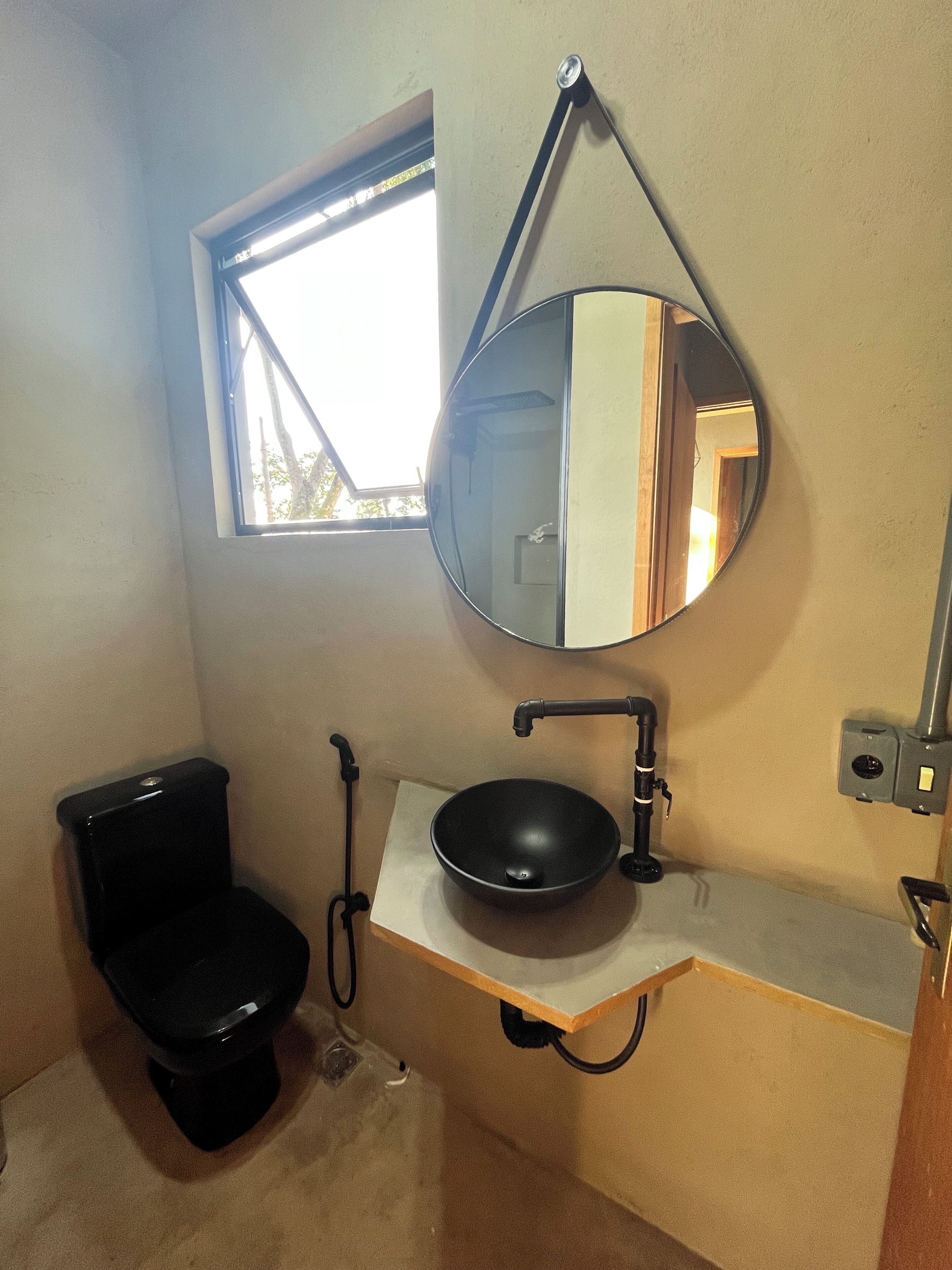 A bathroom with a toilet, a sink, a mirror, and a window.