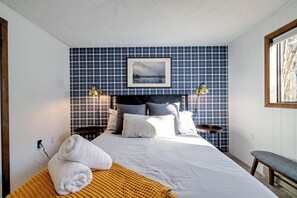 A neatly made bed with white linens, a yellow throw blanket, and two towels. There is a framed picture on the wall above the bed.