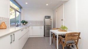 A compact kitchen with white cabinets, a stainless steel refrigerator, a microwave, and a dining table with chairs. - Tambo Lindo- Meaning beautiful inn in Quechua the Inca language of Perú (Smiths Lake)