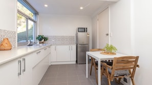 Cocina compacta con armarios blancos, refrigerador de acero inoxidable, microondas y una mesa de comedor con sillas.