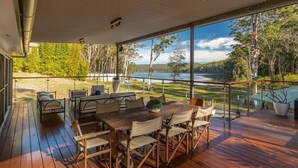 A wooden deck with outdoor furniture, overlooking a lake and trees. - Tambo Lindo- Meaning beautiful inn in Quechua the Inca language of Perú (Smiths Lake)