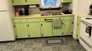 A kitchen with green cabinets, a sink, a stove, and a window with a view of trees.