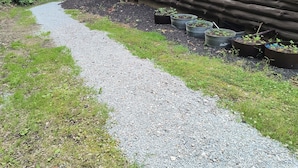 A log cabin with a gravel path leading to the entrance, surrounded by greenery and potted plants.