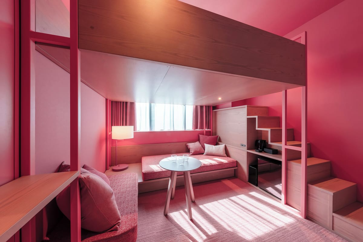 A compact room with a built-in bed, a small table, a desk, and a staircase.